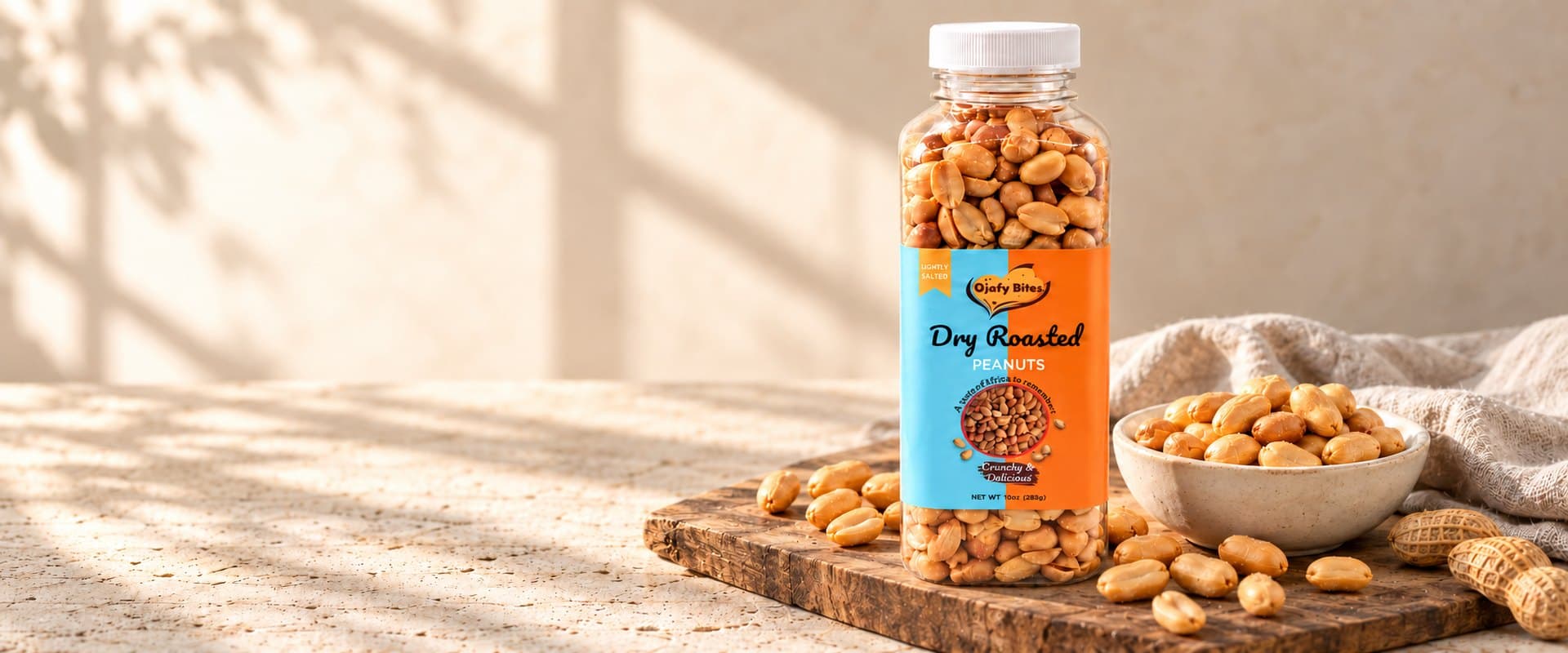 A bottle of Ojafy Bites dry roasted peanuts on a wooden board beside a bowl of peanuts